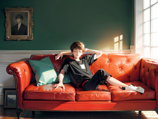 A young European boy leans back on a black sofa?With his eyes closed?